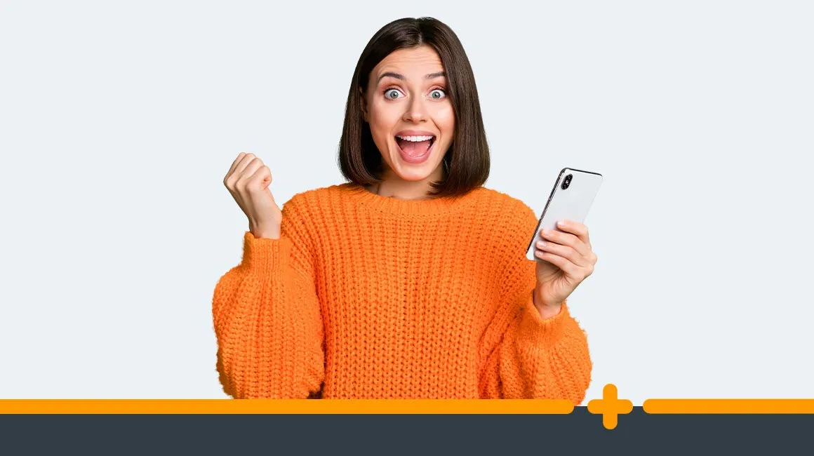 Zachwycona młoda kobieta w pomarańczowym swetrze trzymająca smartfon