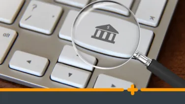 Lupa nad klawiaturą komputerową z ikoną banku, symbolizująca wyszukiwanie ofert finansowych lub porównywanie pożyczek online.